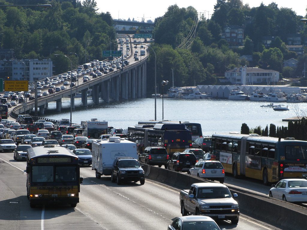 Vehicles moving slowly on a congested highway in Seattle. The highway crosses a narrow river.