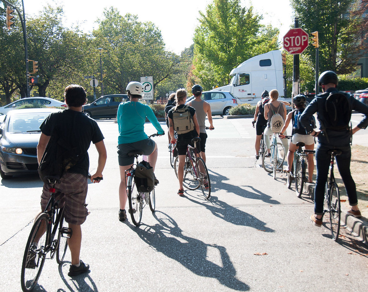 People on bikes waiting at a stop sign to cross a congested intersection