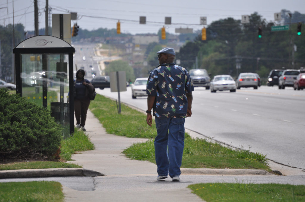 A Black man walks to a bus stop along a multi-lane highway