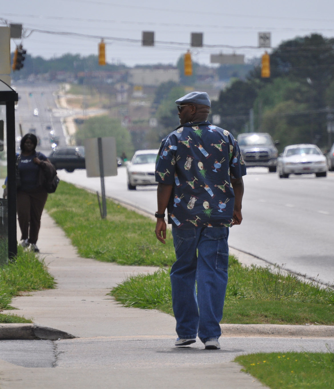 A Black man walks to a bus stop along a multi-lane highway