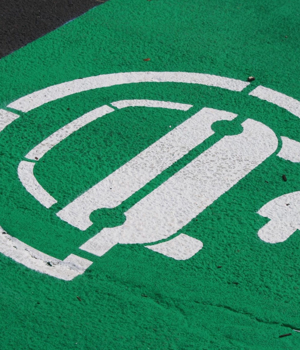 A parking space painted green with a symbol indicating the space is dedicated for EVs