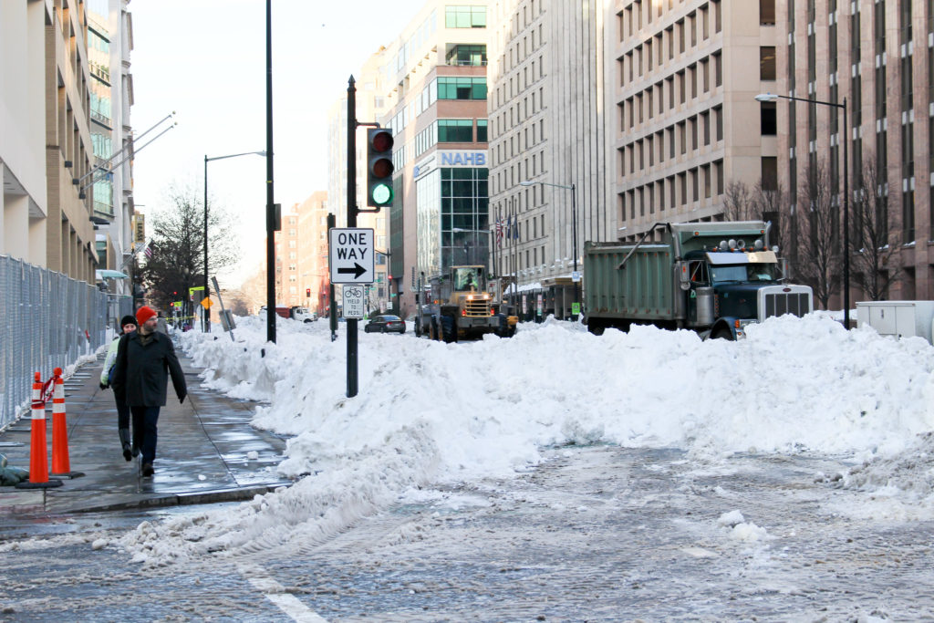 Pedestrians attempt to cross the street next to a pile of snow blocking a one-way lane