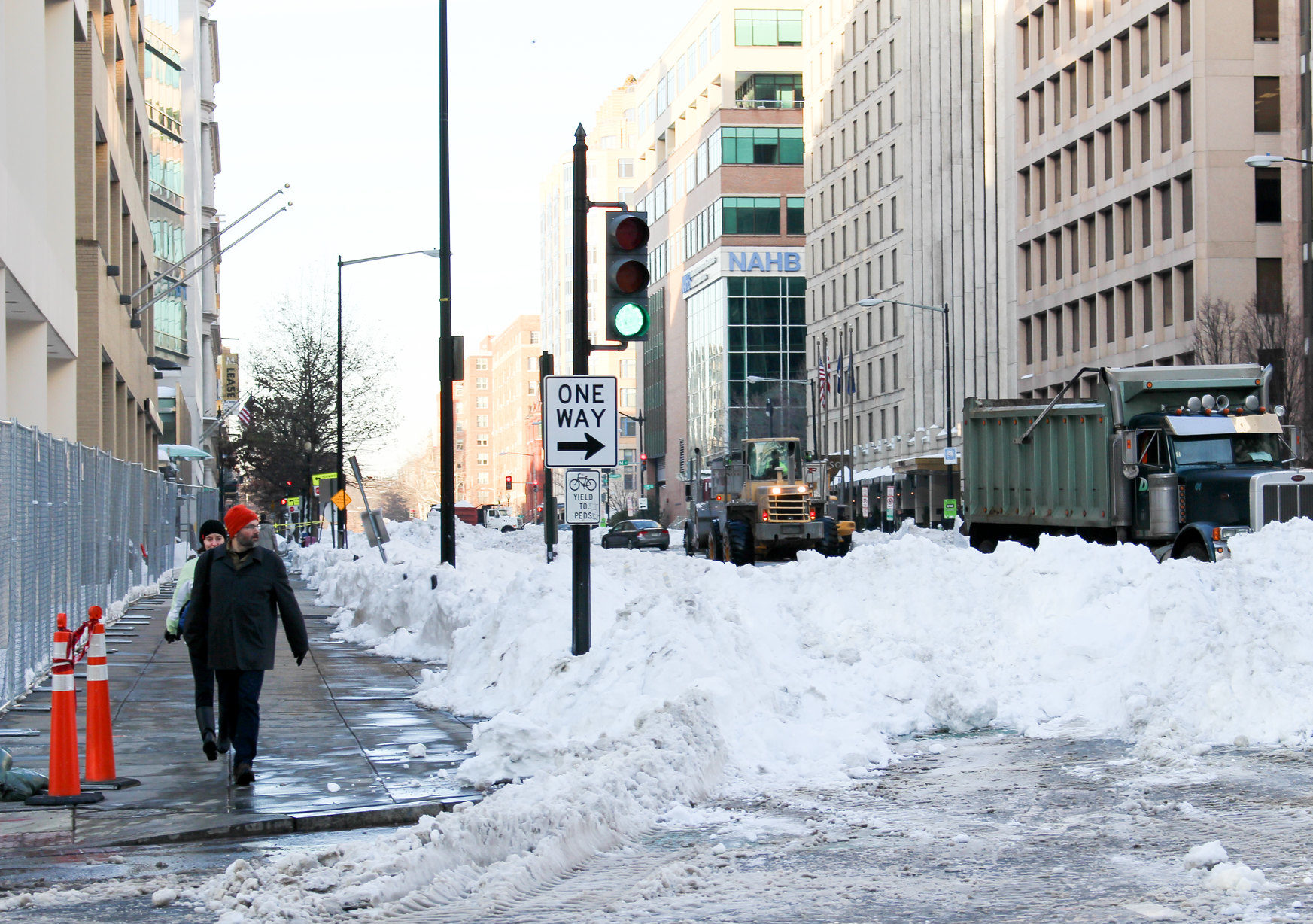 Pedestrians attempt to cross the street next to a pile of snow blocking a one-way lane