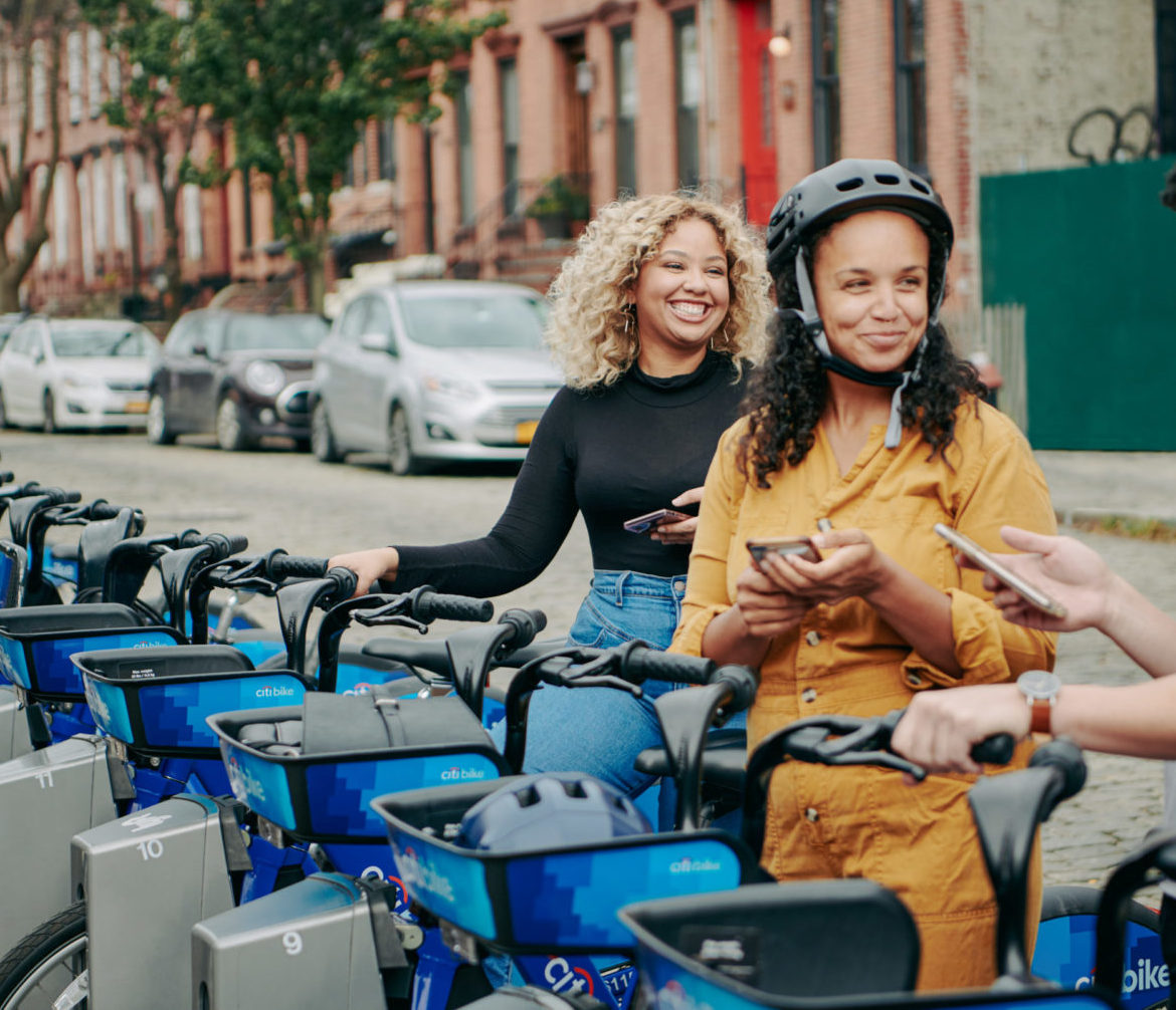 Three people select citibikes at a docking station