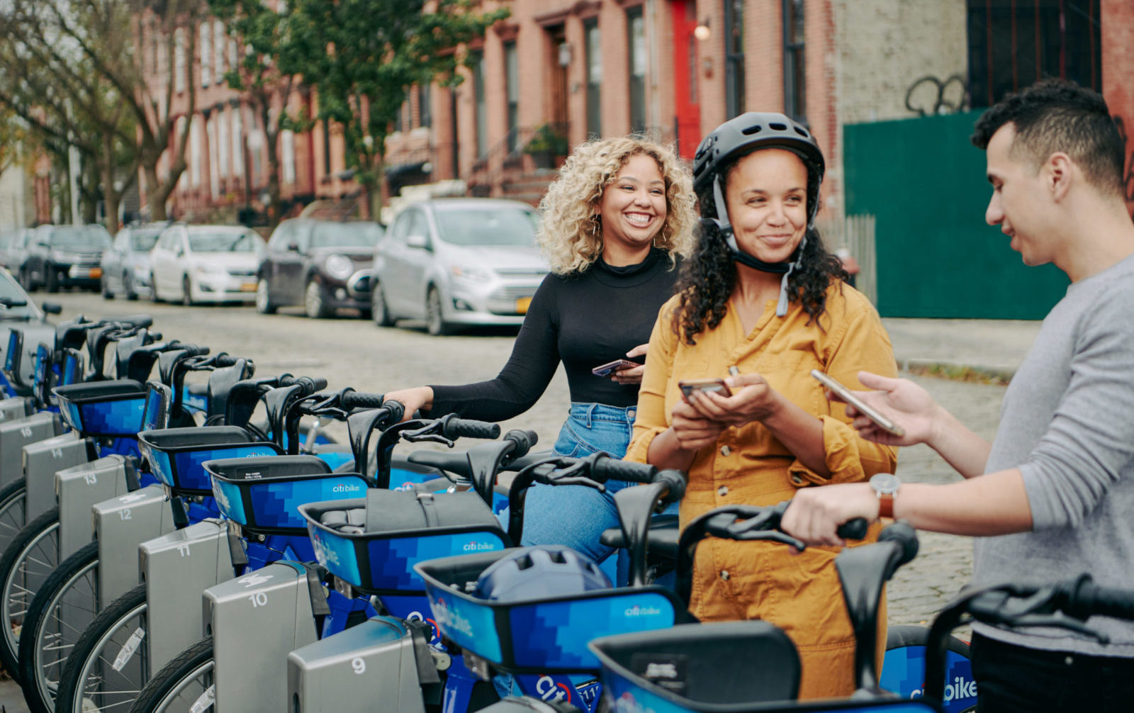 Three people select citibikes at a docking station