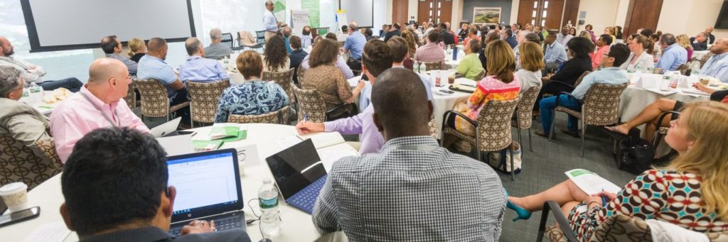 A conference room filled with diverse people taking notes