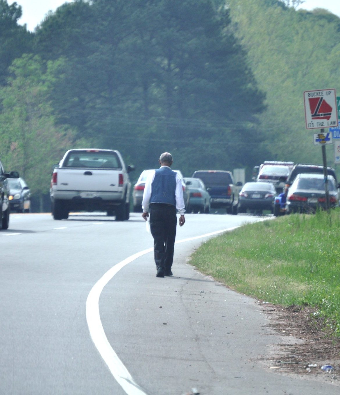 A pedestrian walks along the edge of a road filled with cars.