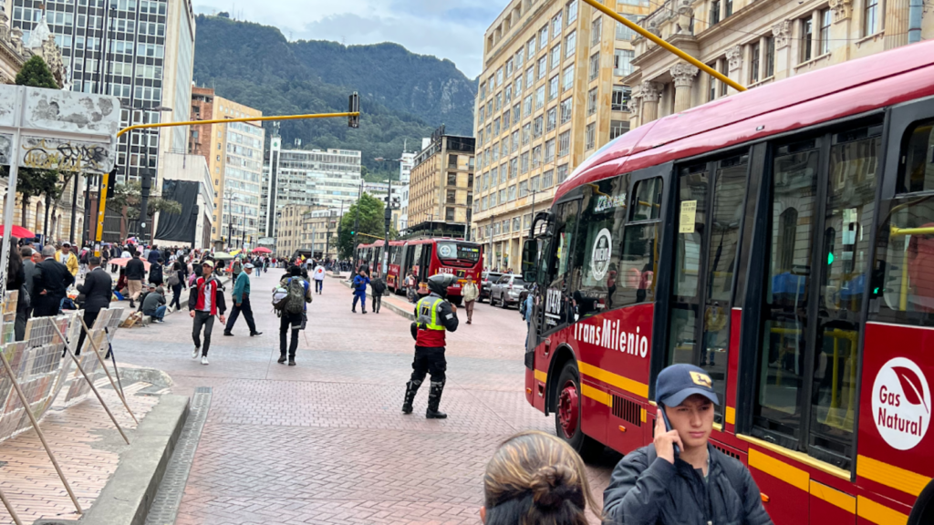 Three TransMilenio buses are waved on by a police officer in a brightly colored vest