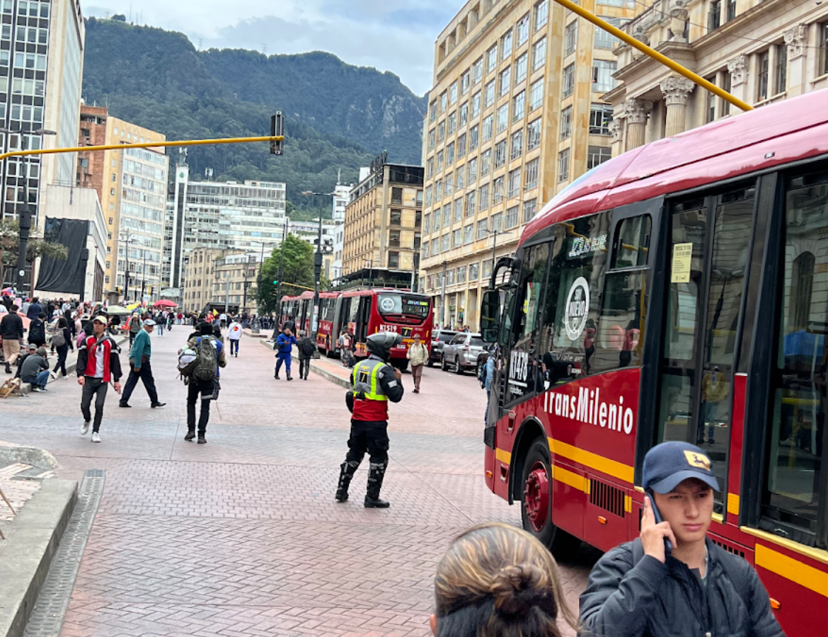 Three TransMilenio buses are waved on by a police officer in a brightly colored vest