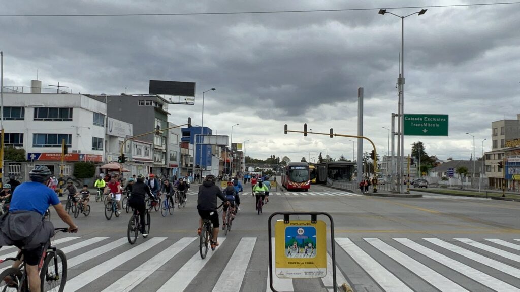 A full range of transportation options are on display: bicyclists and pedestrians in the left lane, a bus in the right lane, and wide crosswalks in the foreground.