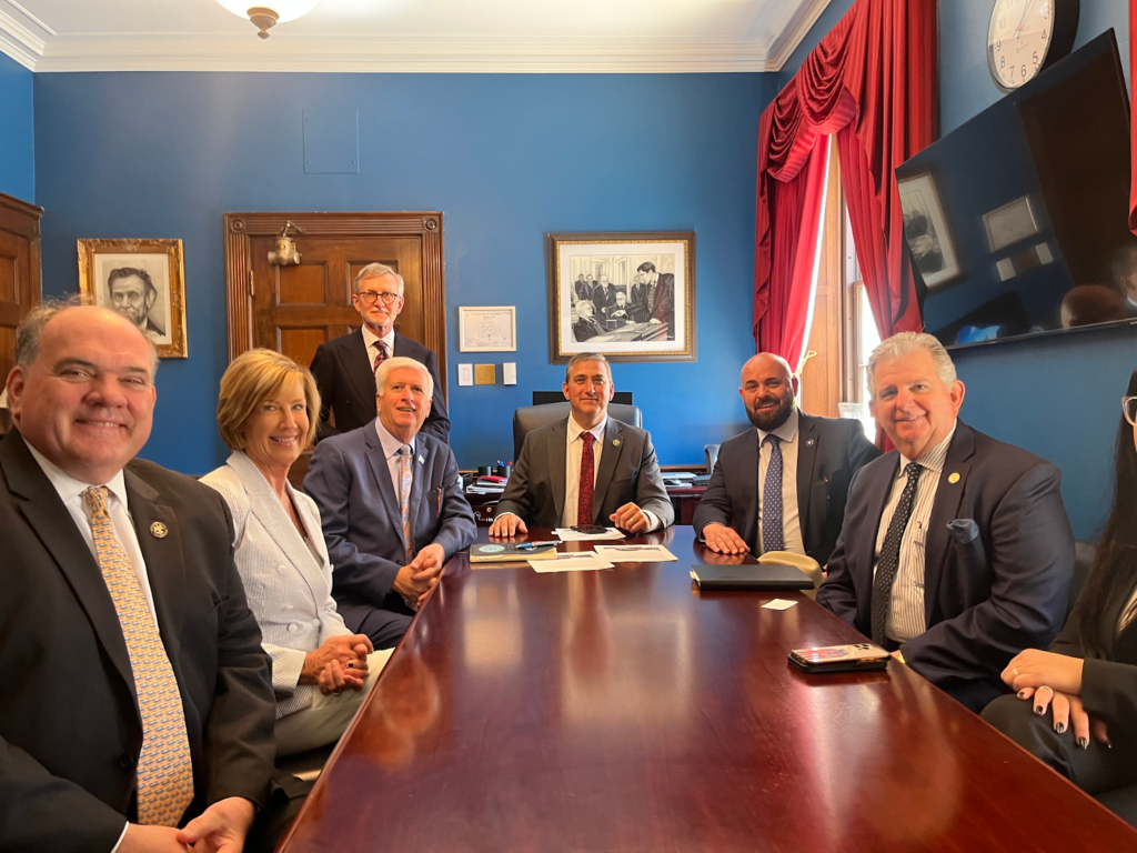 A group of people smile around a shiny wood table in a meeting room