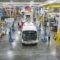Electric buses line up in a brightly lit warehouse with an American flag in the background