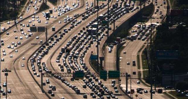 Highway lanes crisscross across an otherwise barren landscape. Rows of tightly clustered cars dot the lanes