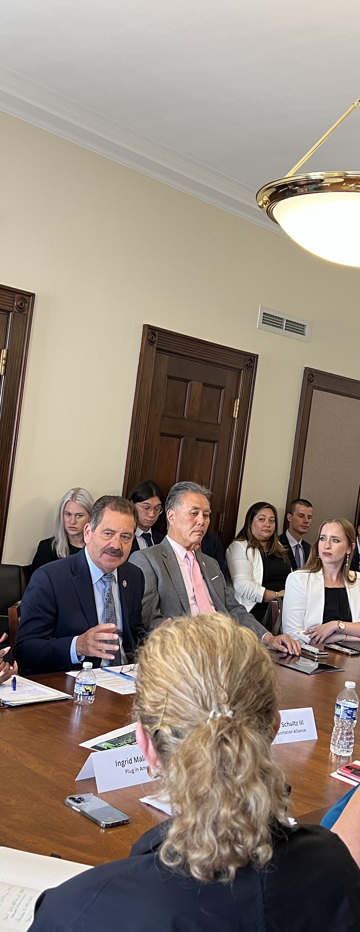Representative Chuy Garcia sits in the center of an oval table, surrounded by advocates and legislatures