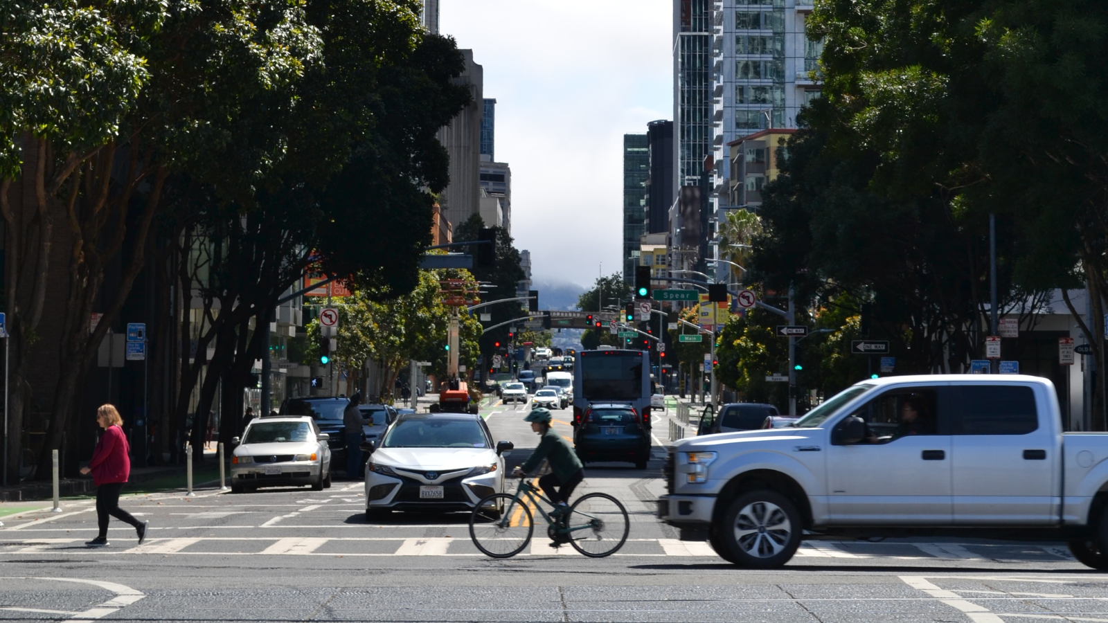 A large truck closely follows a cyclist on a busy roadway in San Francisco