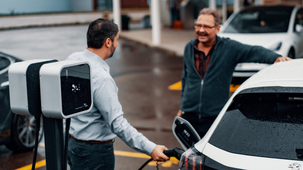 One man charging his white EV while speaking to another man wearing glasses