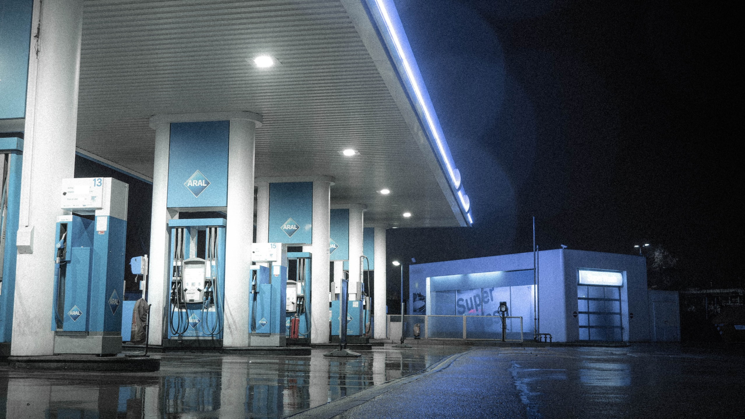 An empty gas station with rows of abandoned power blue pumps glowing with neon lights in the middle of the night