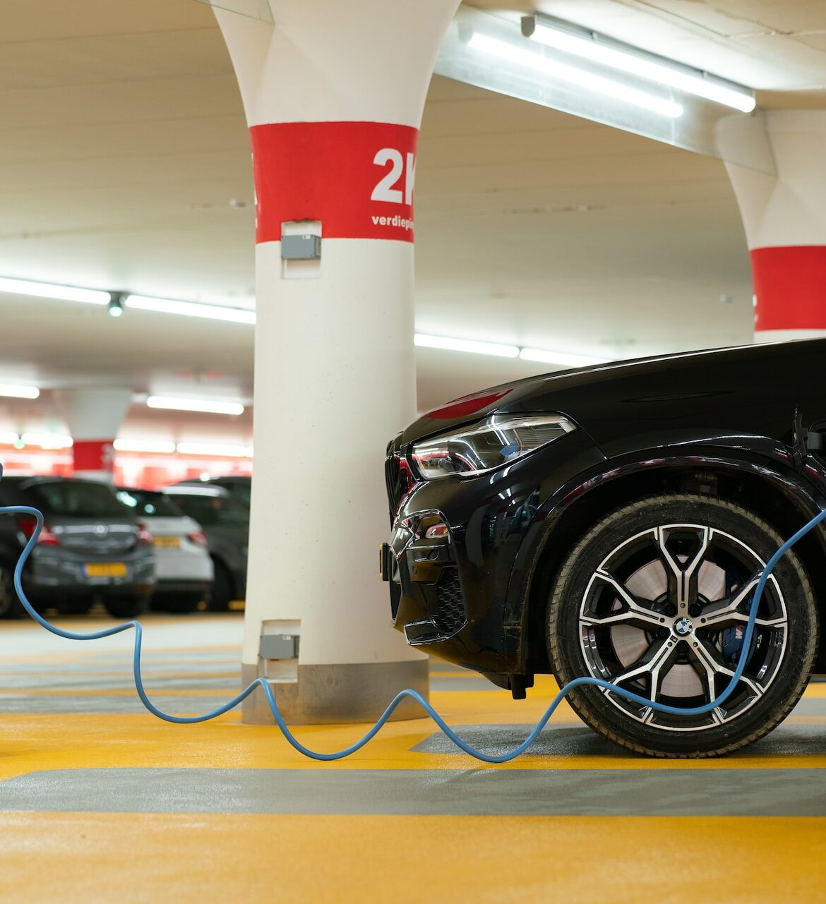 A black SUV is plugged into a charger at a numbered parking spot inside a parking garage.