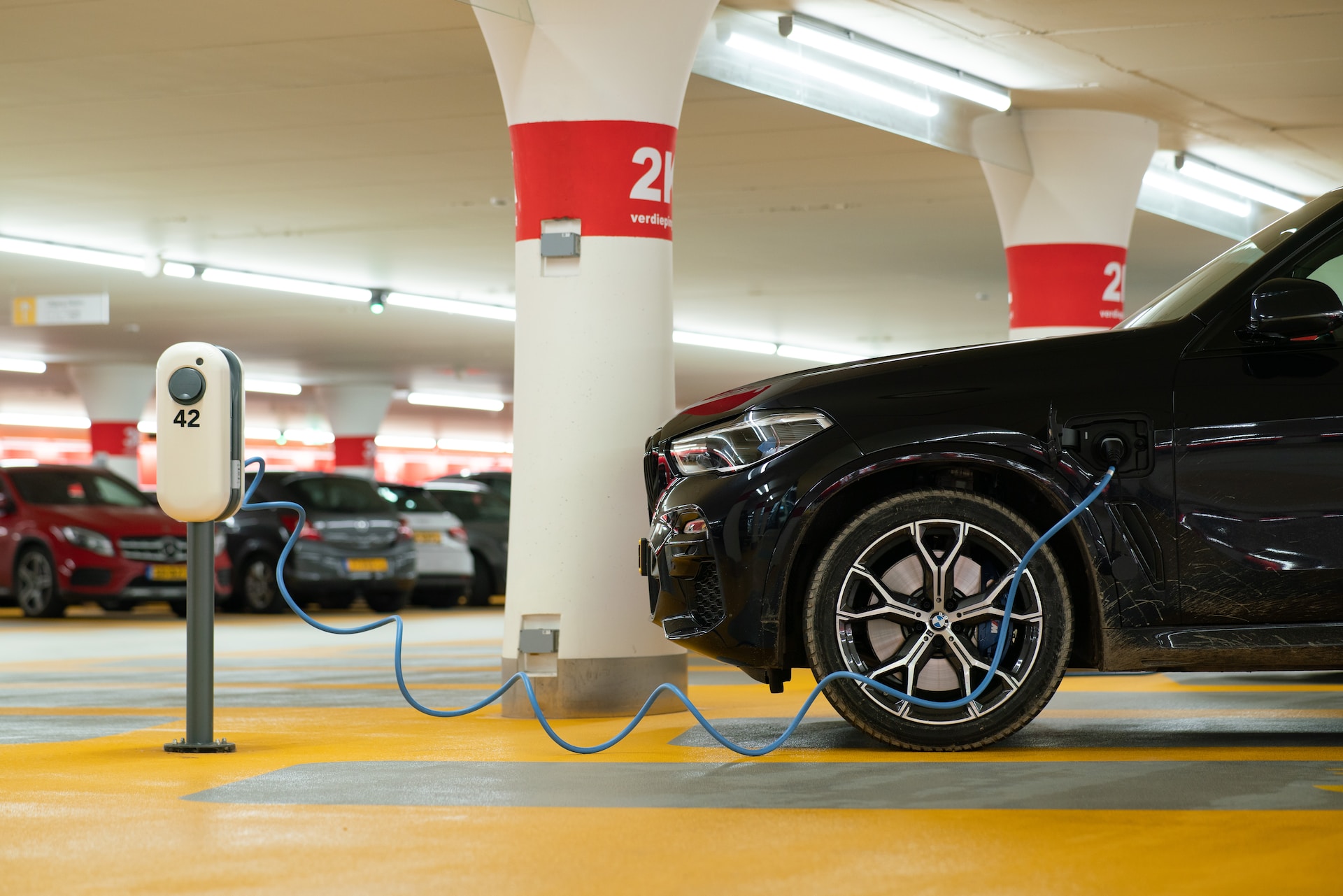 A black SUV is plugged into a charger at a numbered parking spot inside a parking garage.