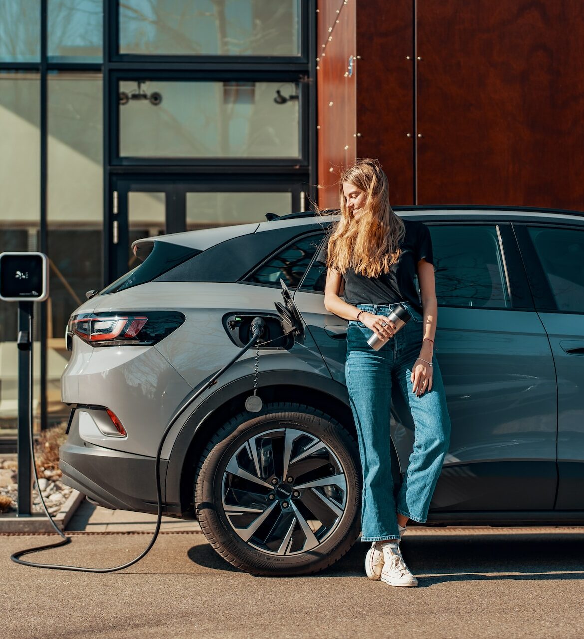 A woman leans against her EV while it charges outside of an apartment building