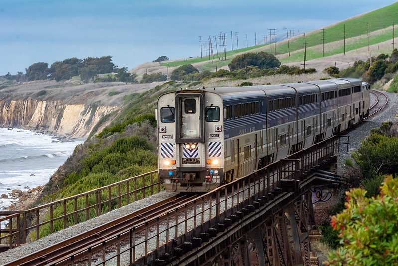 A passenger train crosses a bridge near coastal California cliffs