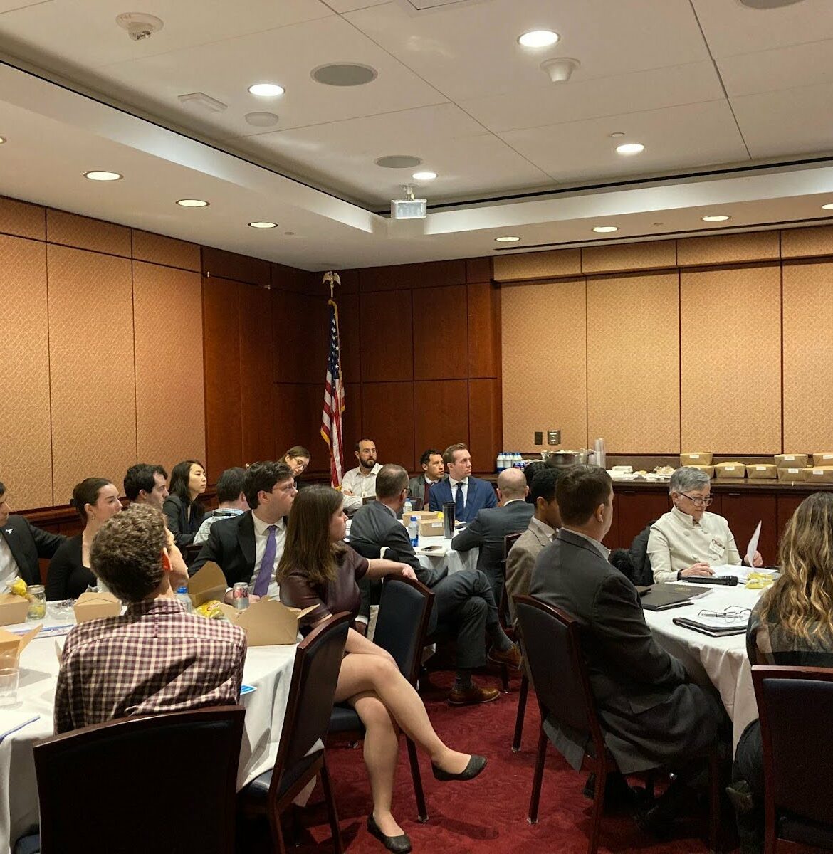 A group of people in formal business attire sits in a conference room listening to a member of the roundtable speak