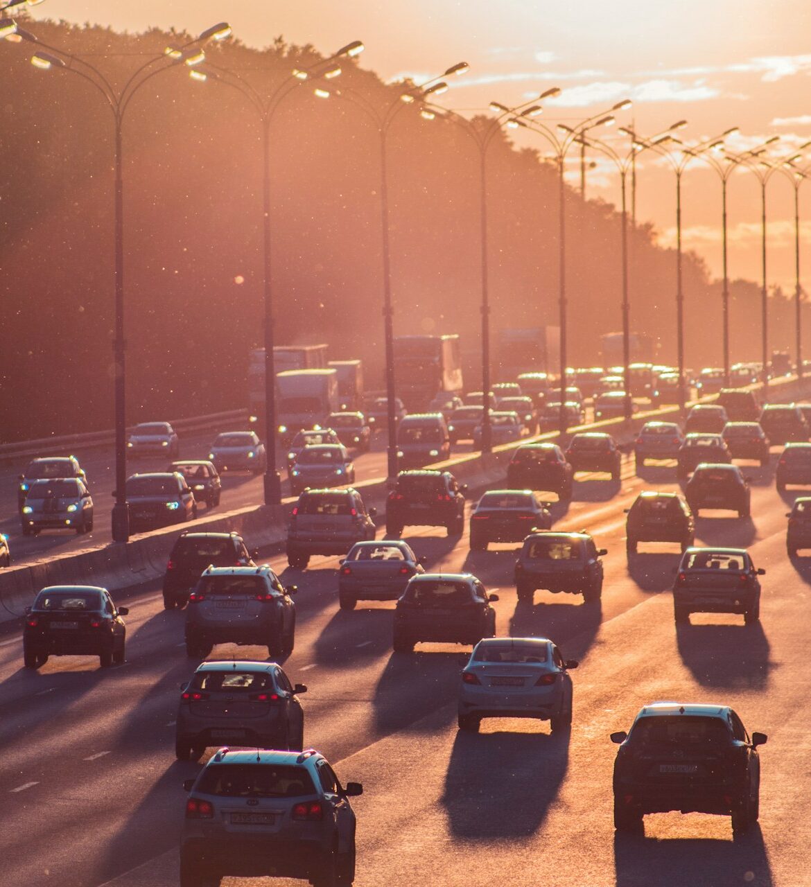 A hazy orange sunset descends over rows and rows of cars traveling down a highway