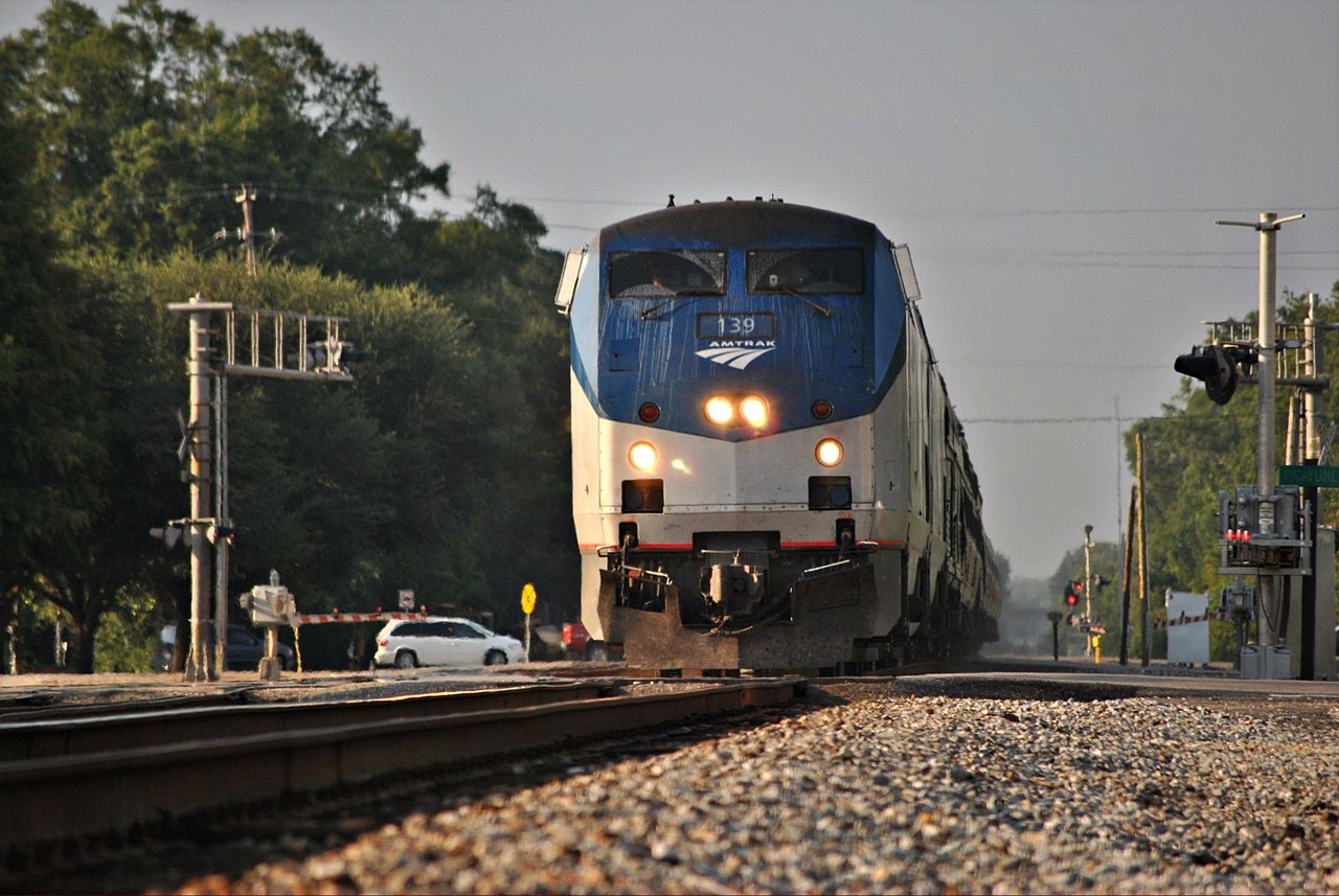 A shiny passenger train chugs down the track in a southern town
