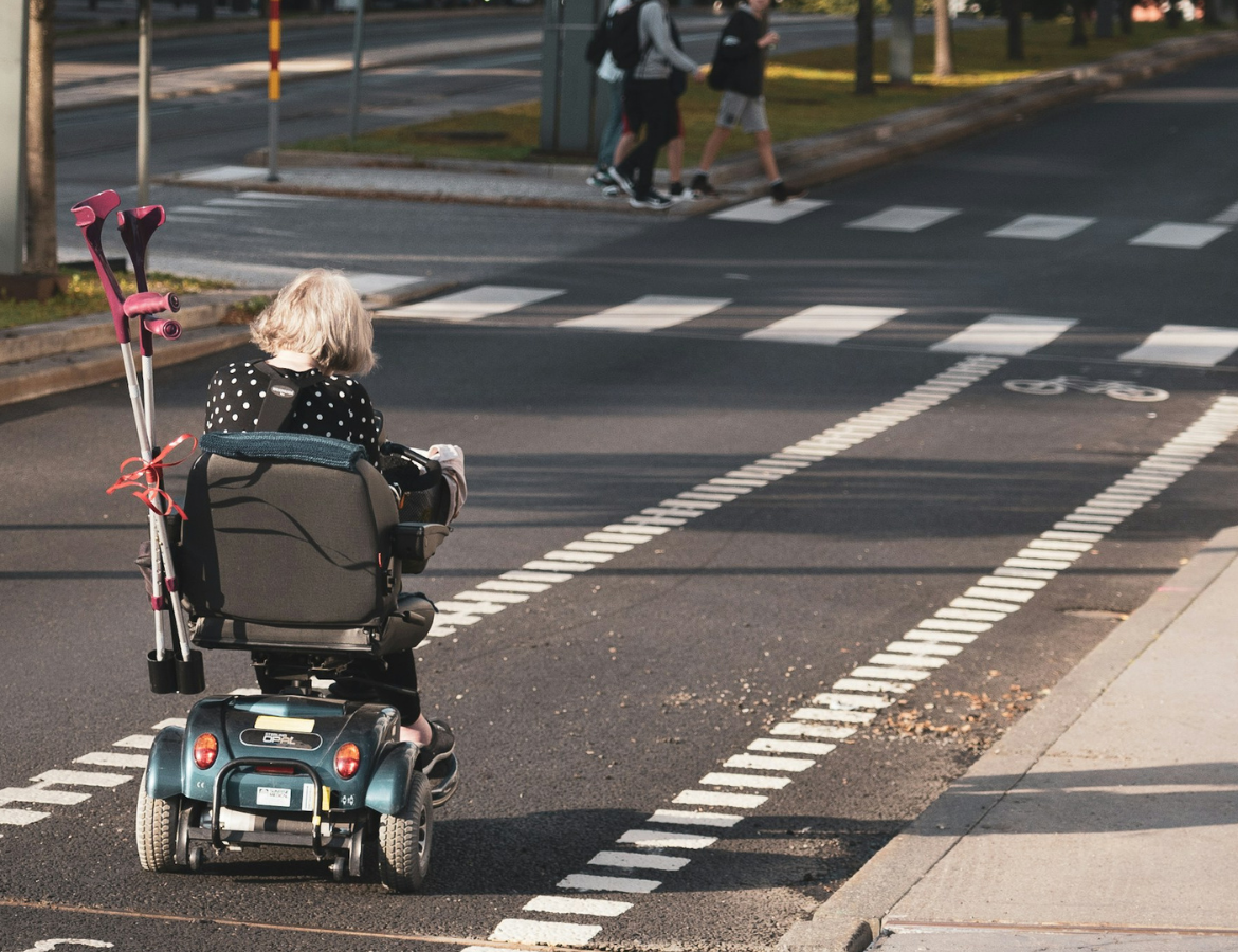 A young child in a wheelchair travels down a bike lane on a narrow, calm street
