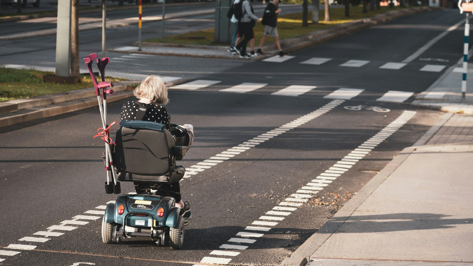 A young child in a wheelchair travels down a bike lane on a narrow, calm street