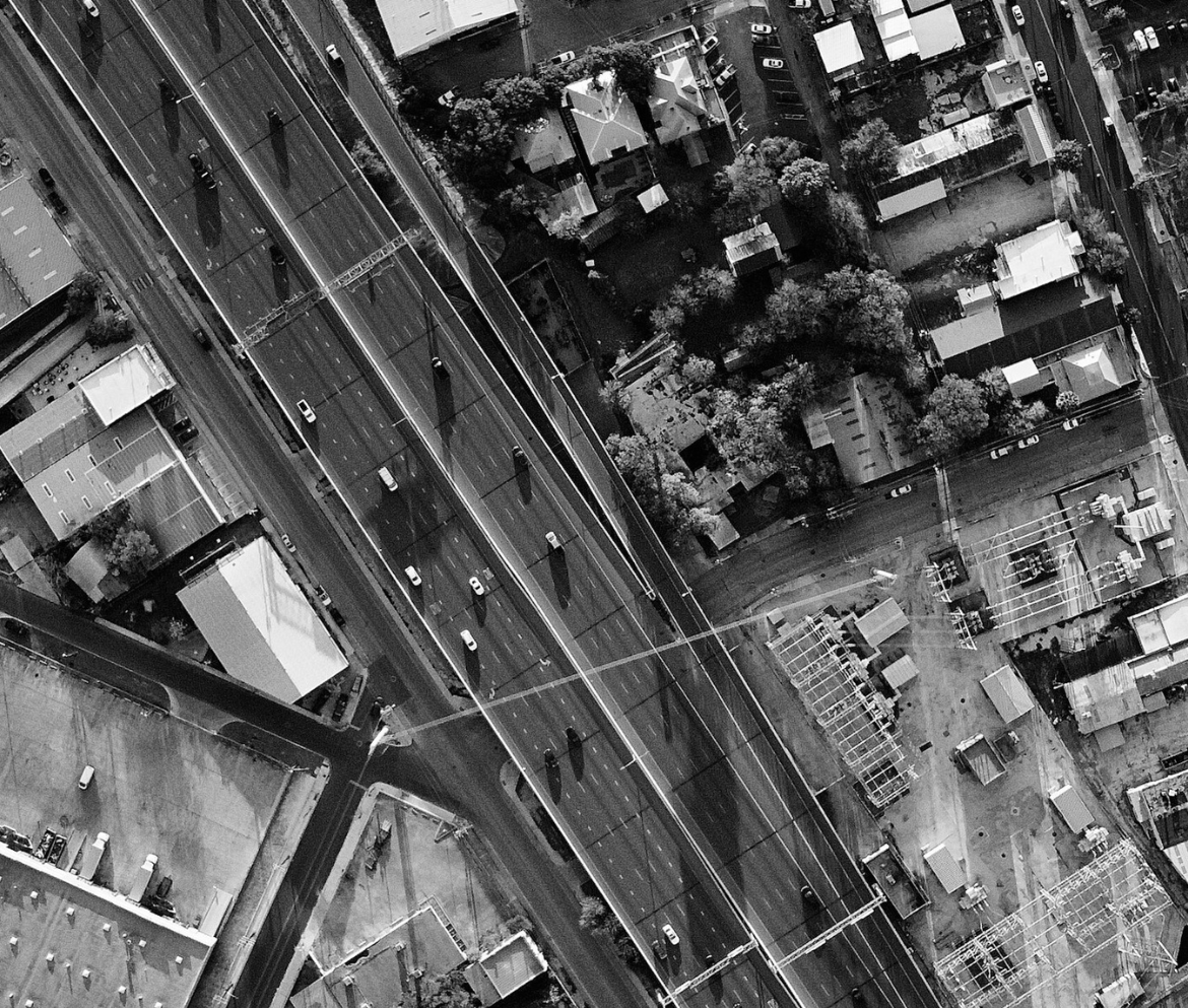 Black and white aerial image of a highway separating a neighborhood from a row of businesses