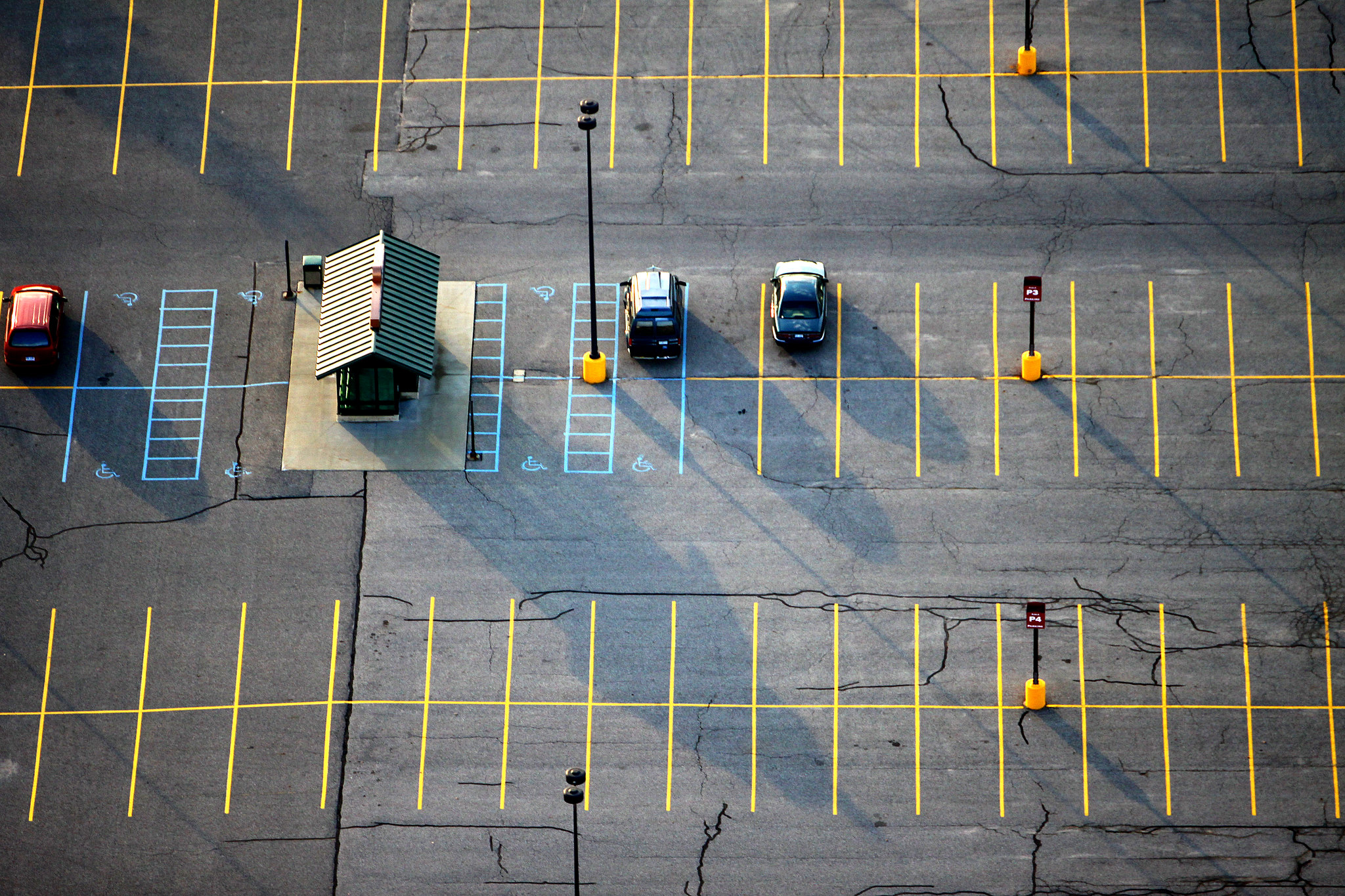 A parking lot hosts three cars and dozens of empty spaces