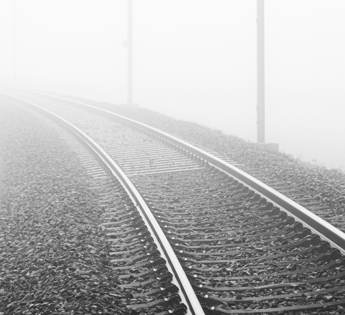 An empty black-and-white train track disappears into the fog