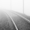 An empty black-and-white train track disappears into the fog