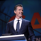 Governor Gavin Newsom wears a blue suit and tie, smiling from a podium