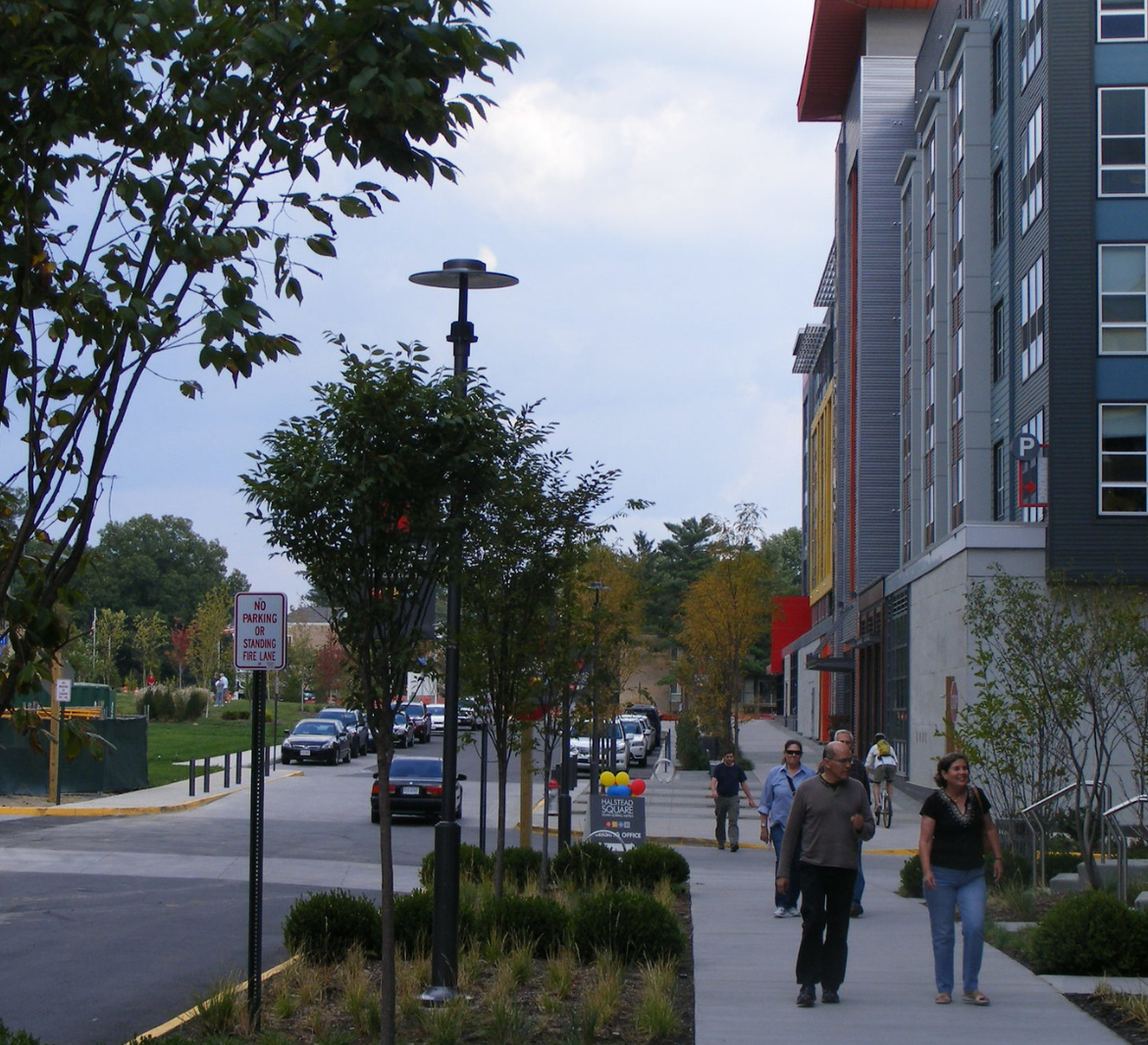 An assortment of people walk down a wide sidewalk near a brightly colored apartment building