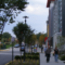 An assortment of people walk down a wide sidewalk near a brightly colored apartment building