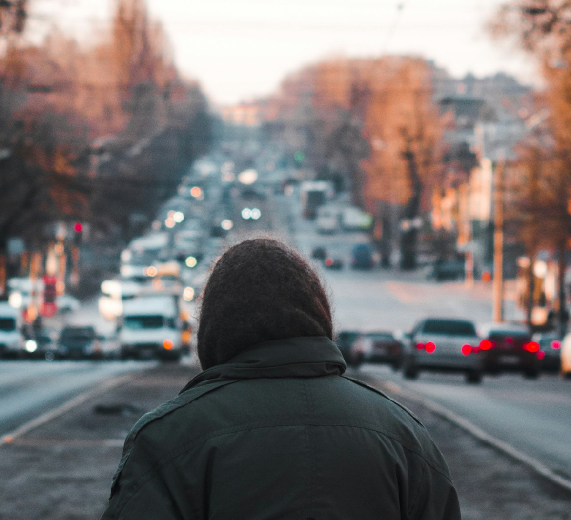 A person wearing a hood and heavy coat faces a busy street filled with cars and stoplights with no way to cross