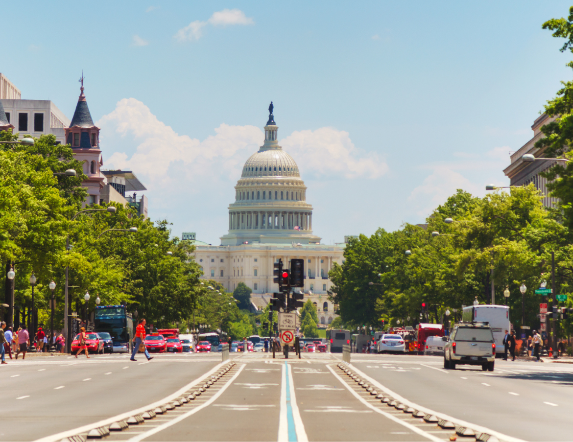 Photograph of a street facing the U.S. Capitol with bike lanes down the middle and pedestrians utilizing a crosswalk