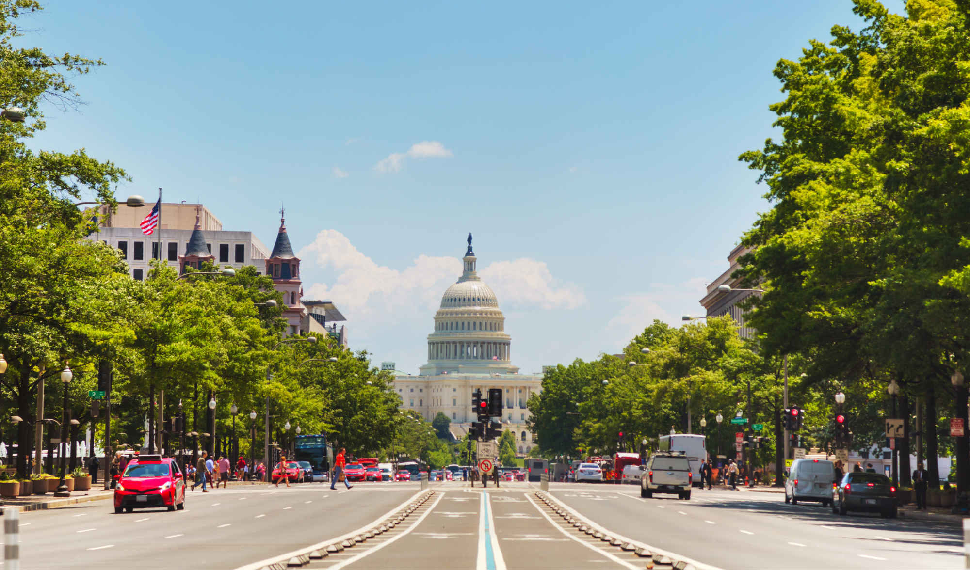 Photograph of a street facing the U.S. Capitol with bike lanes down the middle and pedestrians utilizing a crosswalk