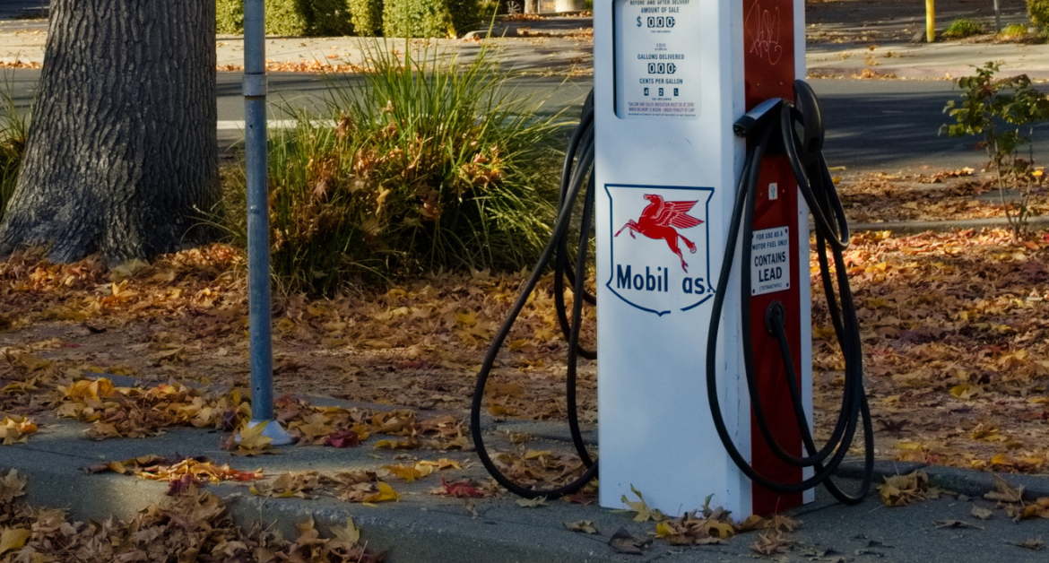 Two EV charging plugs rest on either side of a retrofitted gas pump bearing a faded label