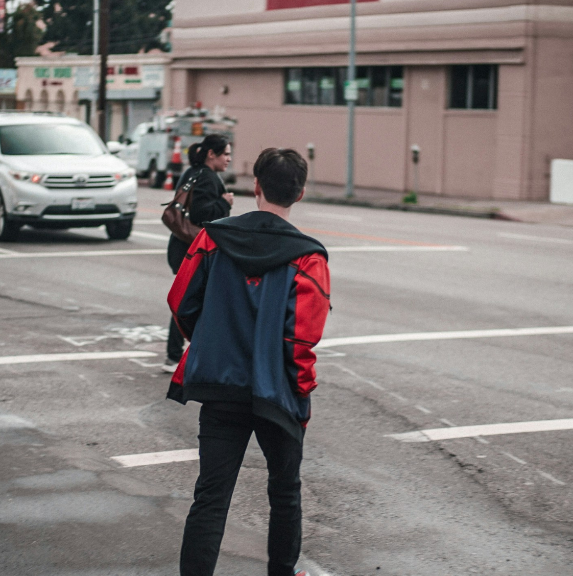 A young man and woman attempt to cross the street on a worn out crosswalk while two cars approach