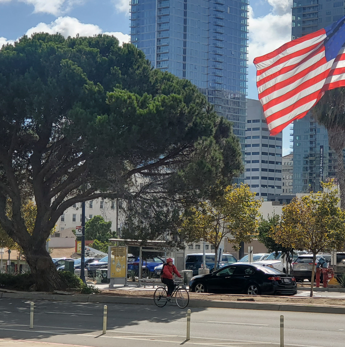 A cyclist passes a bus stop in San Diego, CA as an American flag waves high above his head.