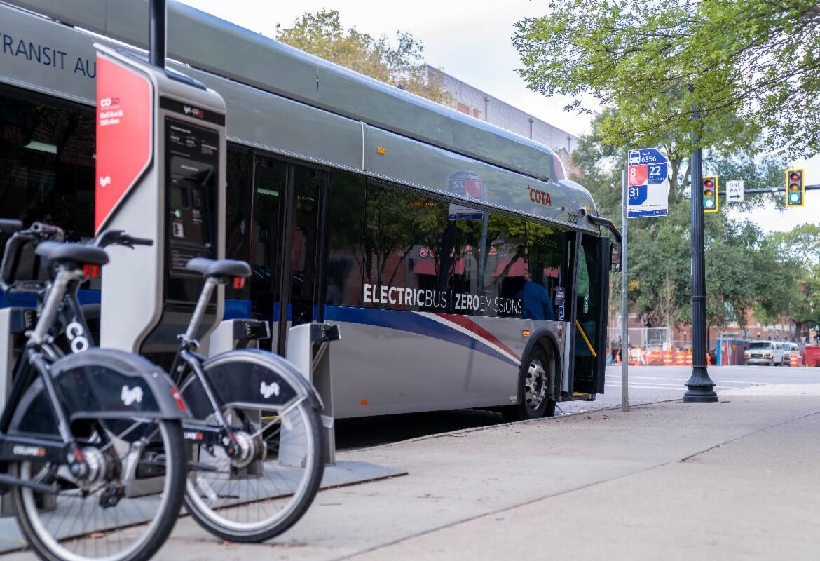 An electric Central Ohio bus arrives at a stop with a nearby bikeshare station