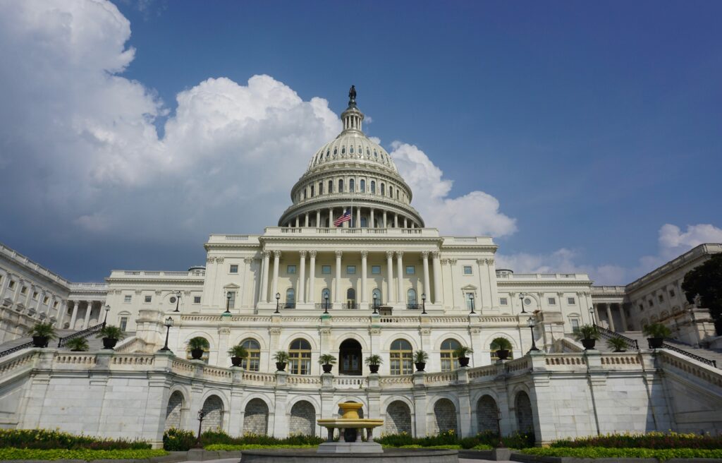 Camera looks up at the white facade that makes up the front of the Capitol building.