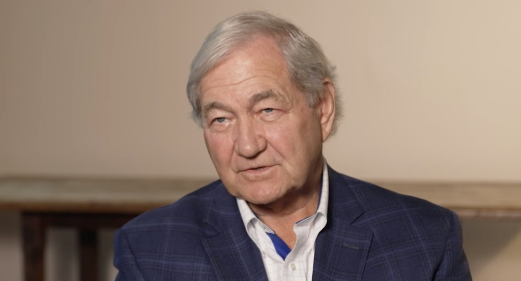 Man in a blue blazer speaking directly to the camera.