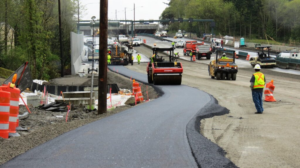 Road construction site where crews are paving a new asphalt path along a large roadway.